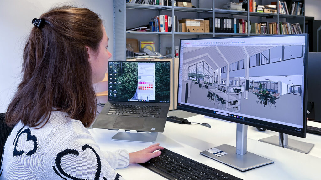 Anouk Dalderop, terwijl ze achter haar computer zit, geeft ze toelichting op het multifunctionele accommodatieproject in Bavel.