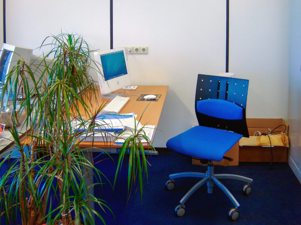 A nostalgic photo of an early Design8 office workspace. The image displays a wooden desk with a classic white Apple iMac G4, a striking blue office chair, paperwork, and a large houseplant, illustrating the atmosphere of the company's early years.
