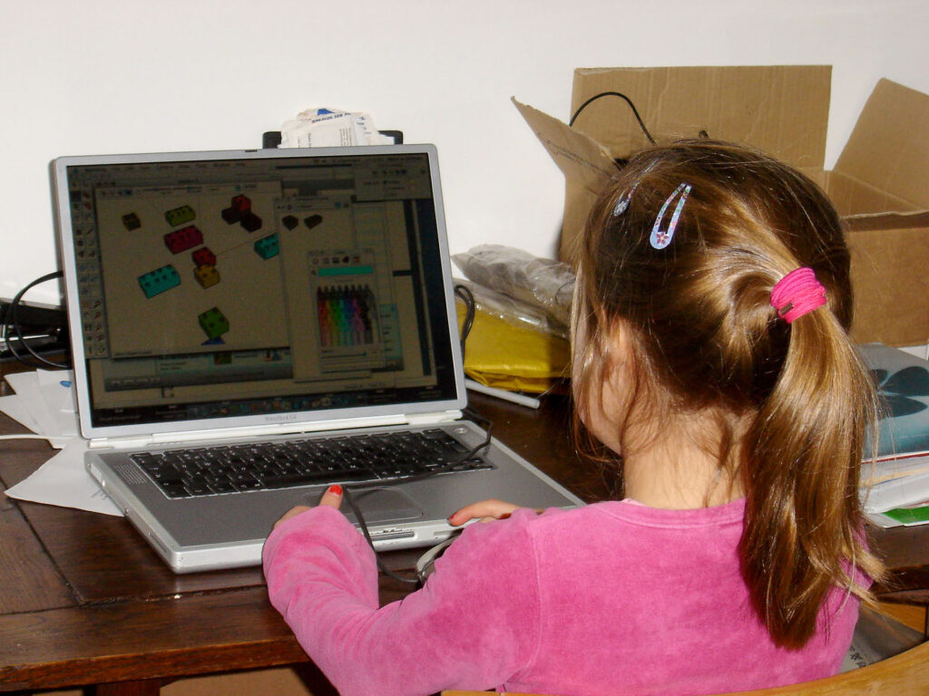 A child working on an old Apple PowerBook laptop, creating a simple block model in a very early version of SketchUp.