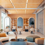 Een fotorealistische 3D-interieurrender van een moderne, luxe kapsalon, gegenereerd met V-Ray 7. De helder verlichte ruimte toont drie wastafels met grote verlichte ovale spiegels, warme houten plafond- en wandpanelen, en een stijlvolle wachtruimte met een organische bank en geribbelde poefs op de voorgrond.