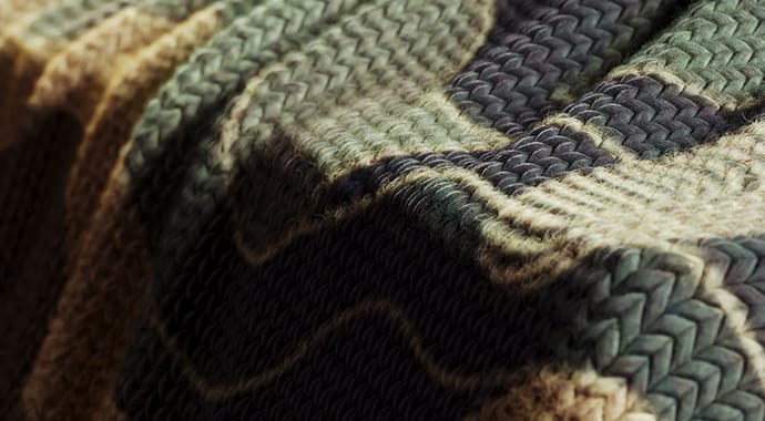 Een extreme close-up 3D-render van een gebreide deken met een ingewikkeld weefpatroon. Dit demonstreert de Chaos Corona Pattern functie, waarmee echte 3D-geometrie (zoals garen) naadloos over een oppervlak wordt herhaald voor ultiem fotorealisme zonder zware geheugenbelasting.