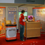 Een overzichtsfoto van een vroege Design8-beursstand ter promotie van SketchUp, voorzien van opvallende gebogen banners. Robert, in een rode polo, zet alles netjes op onze stand op de Bouw & ICT Beurs 2006.