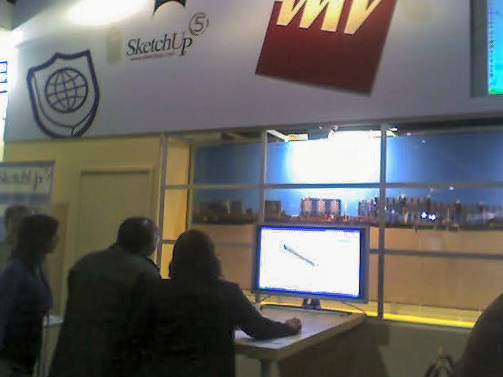 Bezoekers bekijken aandachtig een demonstratie van SketchUp versie 5 op een computerscherm bij de VMV beursstand. Een nostalgisch beeld dat de vroege evolutie van 3D-software markeert.