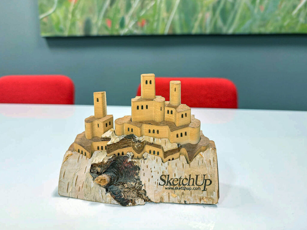 Een gedetailleerd houten schaalmodel van een kasteeldorp, uitgesneden uit een massief blok berkenhout met daarop het klassieke SketchUp logo. Een uniek verzamelobject uit het Design8 archief.