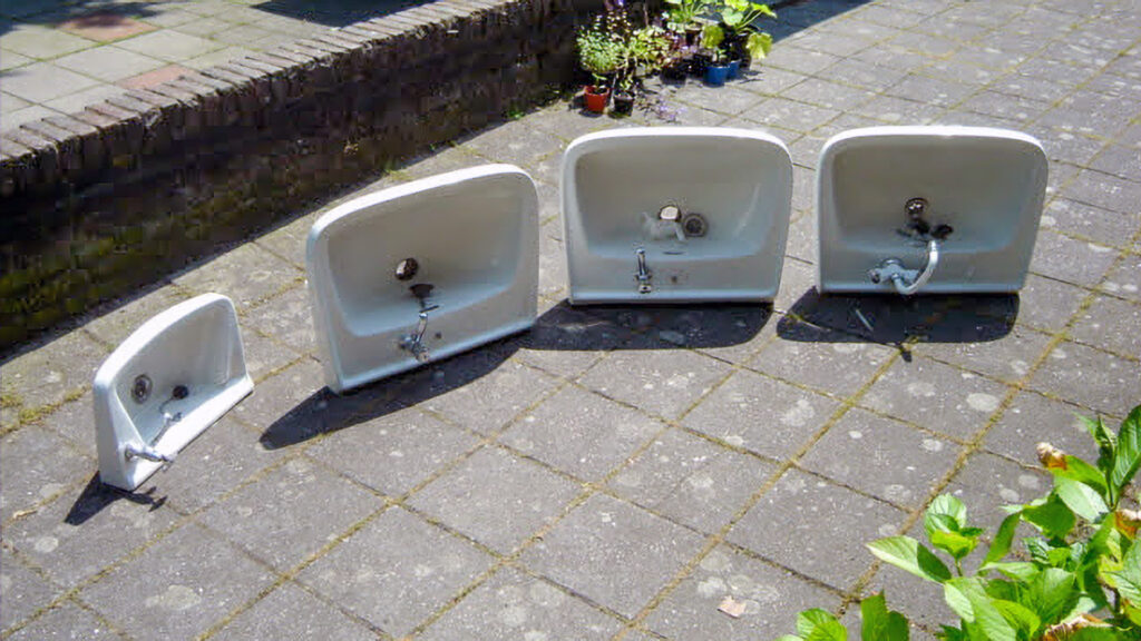 Een reeks van vijf witte keramische wasbakken in verschillende formaten, uitgestald op een buitenterras.