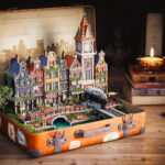 Een magische 3D-render van een vintage koffer die openstaat, met daarin een zeer gedetailleerde, miniatuur Europese grachtenstad inclusief brug, klokkentoren en stoomtrein. Deze hero-afbeelding toont de kracht van V-Ray 7 voor complexe M&E visualisaties.