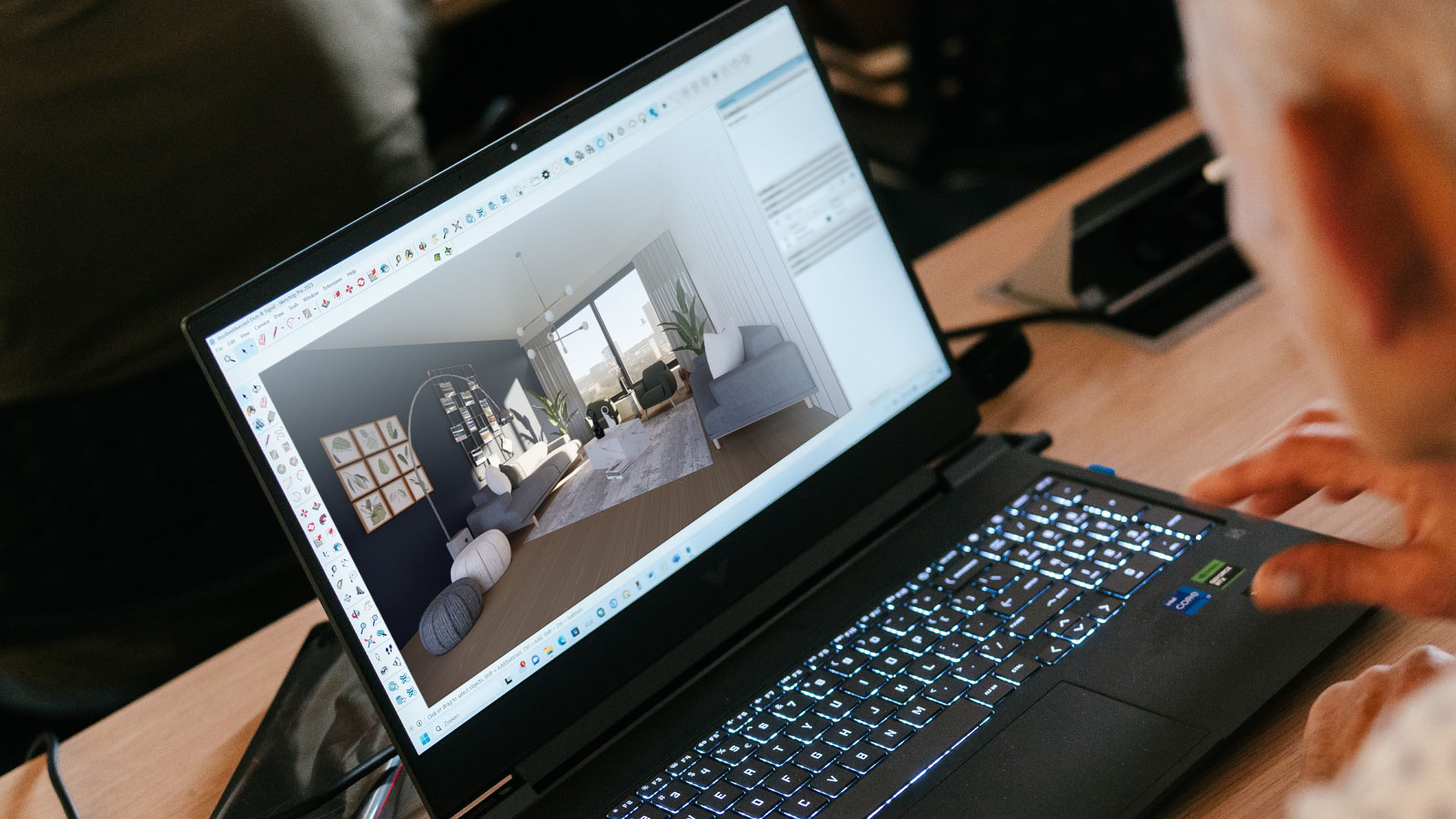 Een professional kijkt over de schouder mee naar een laptop waarop gewerkt wordt aan een 3D-interieurontwerp in SketchUp. Het beeldscherm toont een sfeervol, realistisch belicht 3D-model van een moderne woonkamer met meubilair en grote ramen.