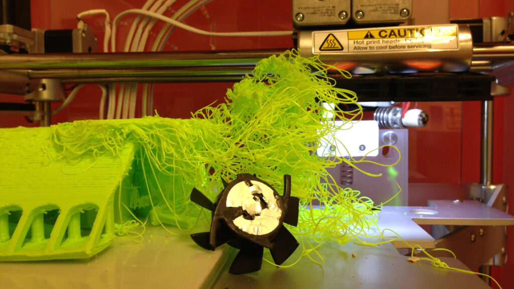 Foto van een 3D printer waarbij de printkop en ventilator is afgebroken, waardoor er een grote plastic brei is ontstaan.