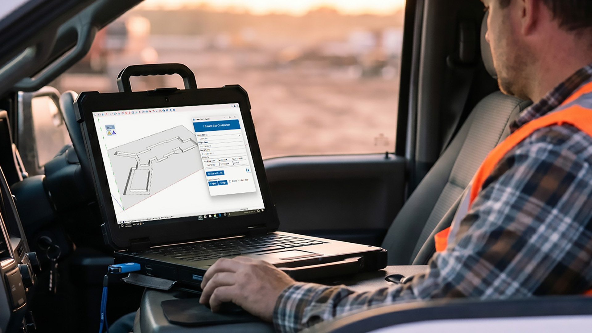 Een aannemer in de cabine van een truck gebruikt een robuuste laptop waarop gespecialiseerde aannemerssoftware met een 3D-ontwerp van een sleuvennetwerk zichtbaar is.