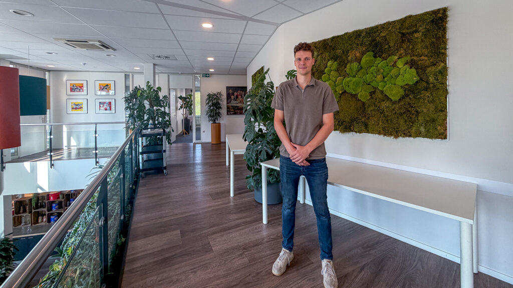 Stedenbouwkundig ontwerper Rick van der Burgt staat in de lichte, moderne gang van het kantoor van Buro Waalbrug, naast een grote decoratieve wand van groen mos.