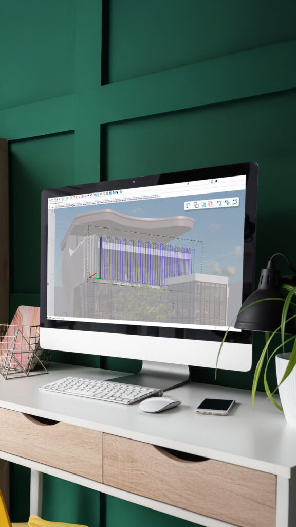 Een verticale monitor op een bureau toont de SketchUp 2027 interface. Op het scherm is een 3D-gebouw zichtbaar waarbij een selectiekader ('core procedure') actief is rondom de verticale gevelbekleding. Focus: SketchUp 2027, core procedure, selectiekader, 3D modelleren, architectuur ontwerp.